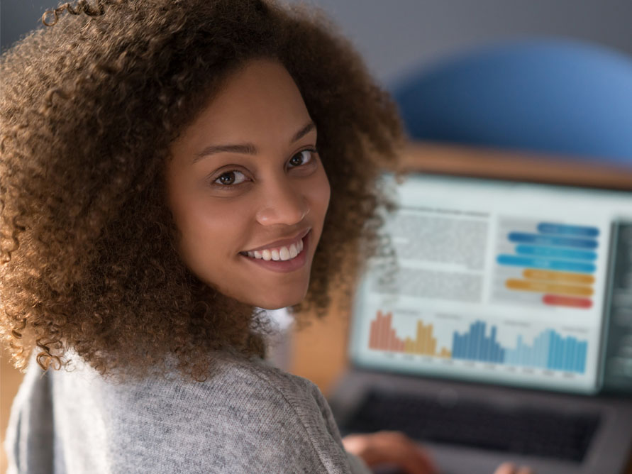 Student sitting at laptop with charts looking back at camera