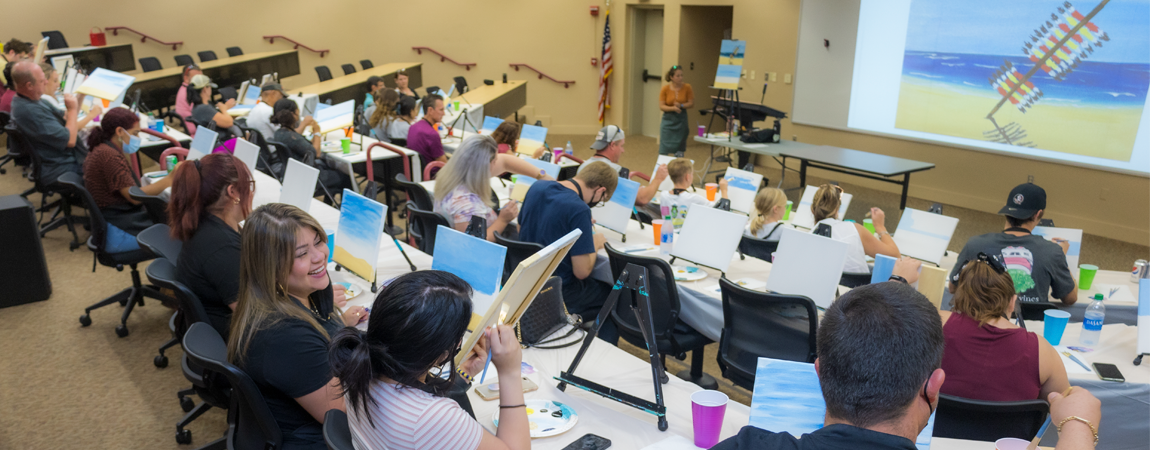 First year students and their family woking on a painting project of the FSU spear in the sand image
