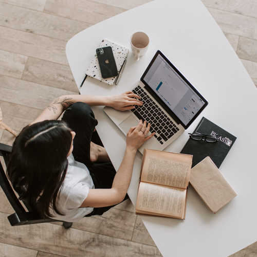Overhead shot of female student typing at a computer with books around her