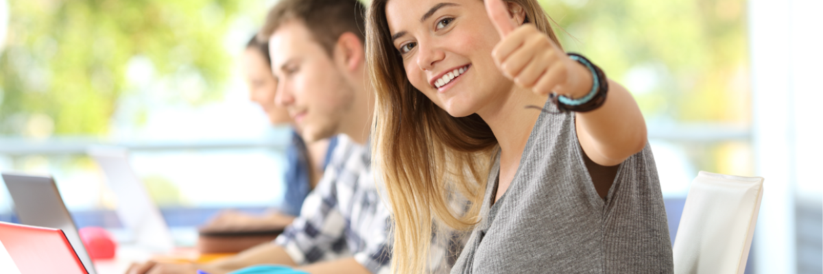 Girl at desk with students and thumbs up sign